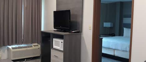 Een hotelkamer met een flatscreen televisie op een standaard, een magnetron, een klein prullenbakje en een bed met witte beddengoed.