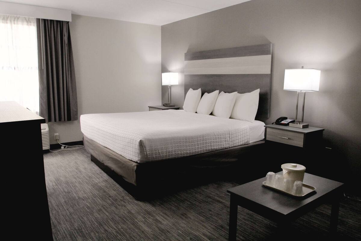 A hotel room with a large bed, two bedside tables with lamps, a small table with a tray, and a window with curtains.