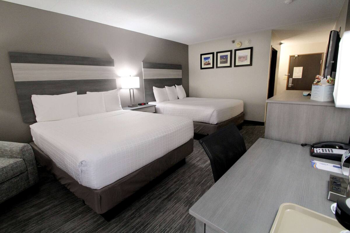 A hotel room with two beds, a desk, a chair, a desk lamp, a phone, and a TV.