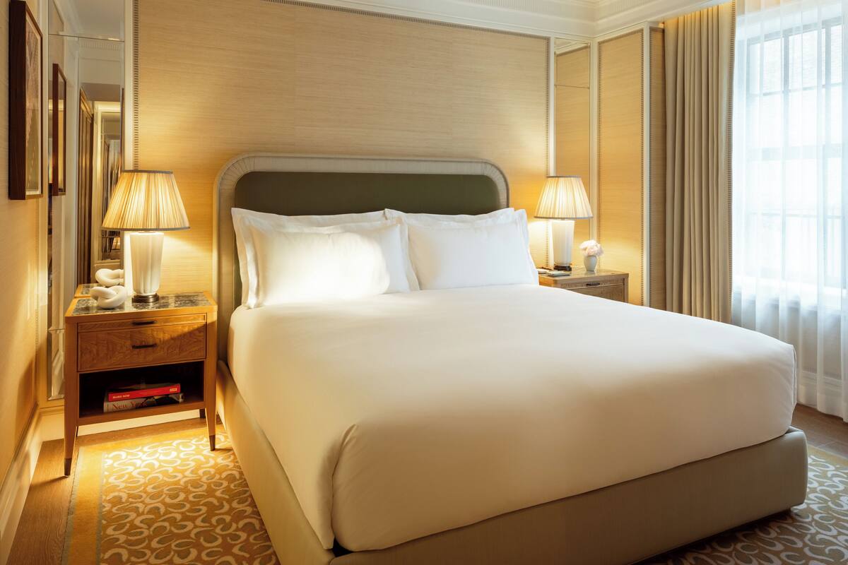 A large bed with a headboard, two bedside tables with lamps, a mirror, and a patterned rug.