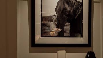 A framed photograph of an elephant on a wall above a dining table with a candle, wine glasses, and a lamp.