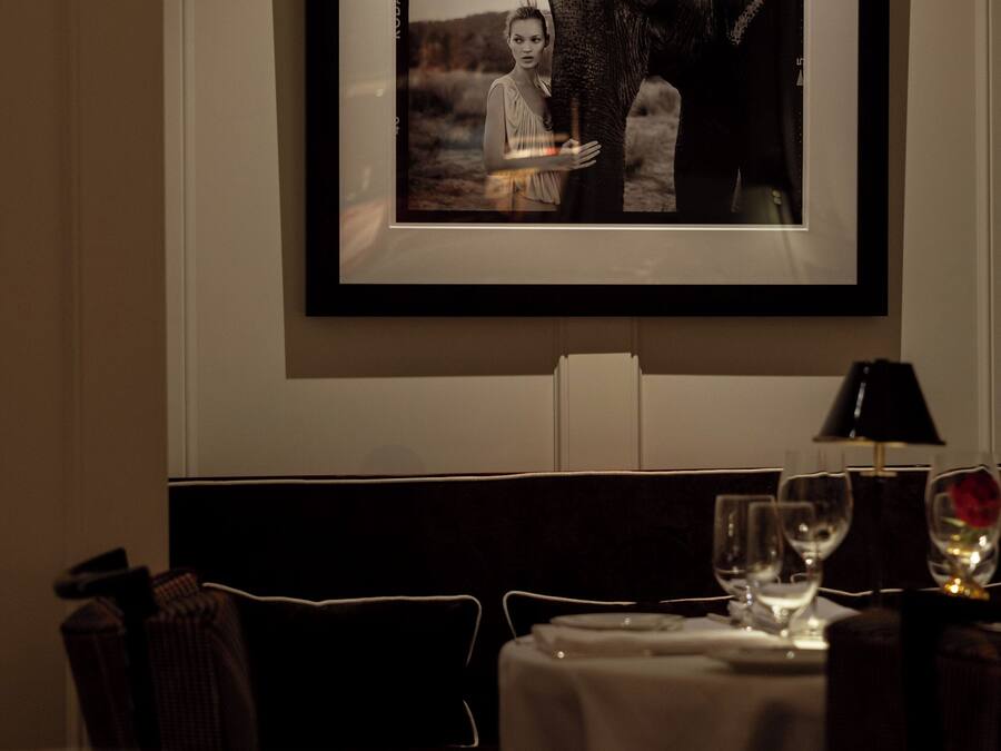 A framed photograph of an elephant on a wall above a dining table with a candle, wine glasses, and a lamp.