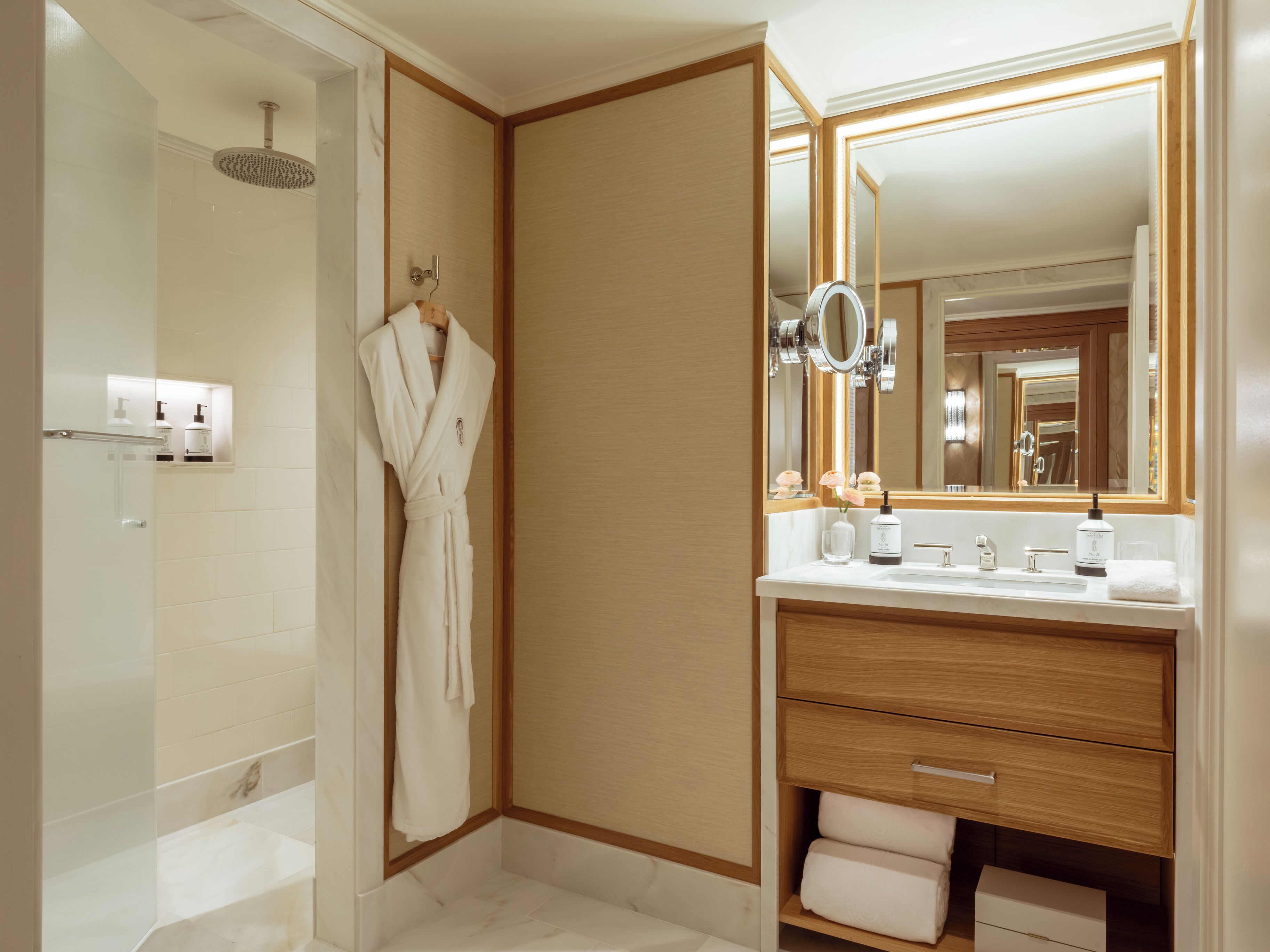 Un baño moderno con cabina de ducha, una bata colgada en un perchero, un tocador con espejo y un estante para toallas.