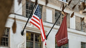 A hotel entrance with an American flag and a red banner, a man in uniform, and potted plants. - The Surrey A Corinthia Hotel (New York)