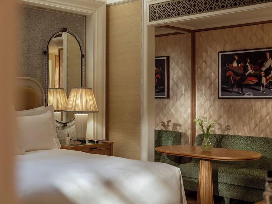 A hotel room with a large bed, a bedside table with lamps, a green sofa, and a small table with a vase.