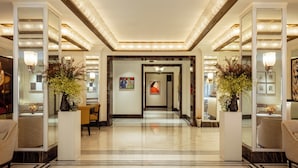 A spacious, well-lit hallway with marble flooring, flanked by large mirrors and decorative vases. - The Surrey A Corinthia Hotel (New York)