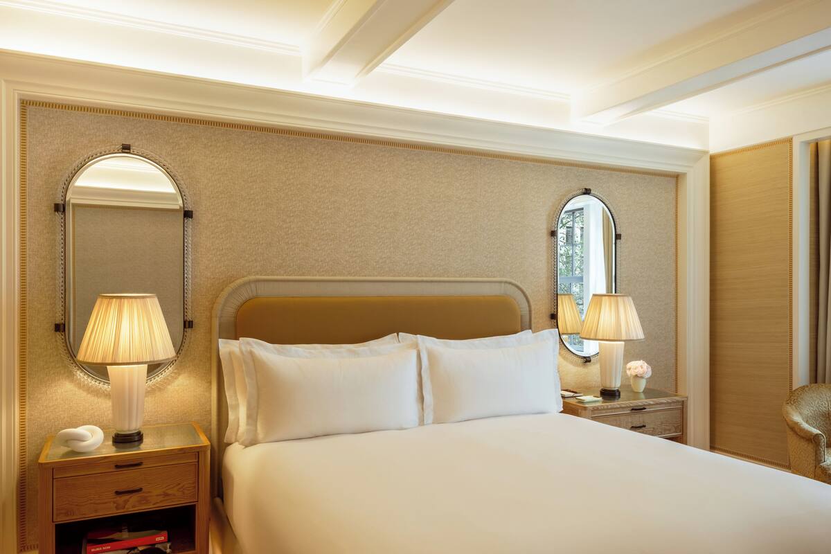 A hotel room with a large bed, two bedside tables with lamps, a mirror, and a small bedside table with a vase.