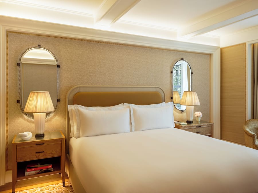 A hotel room with a large bed, two bedside tables with lamps, a mirror, and a small bedside table with a vase.