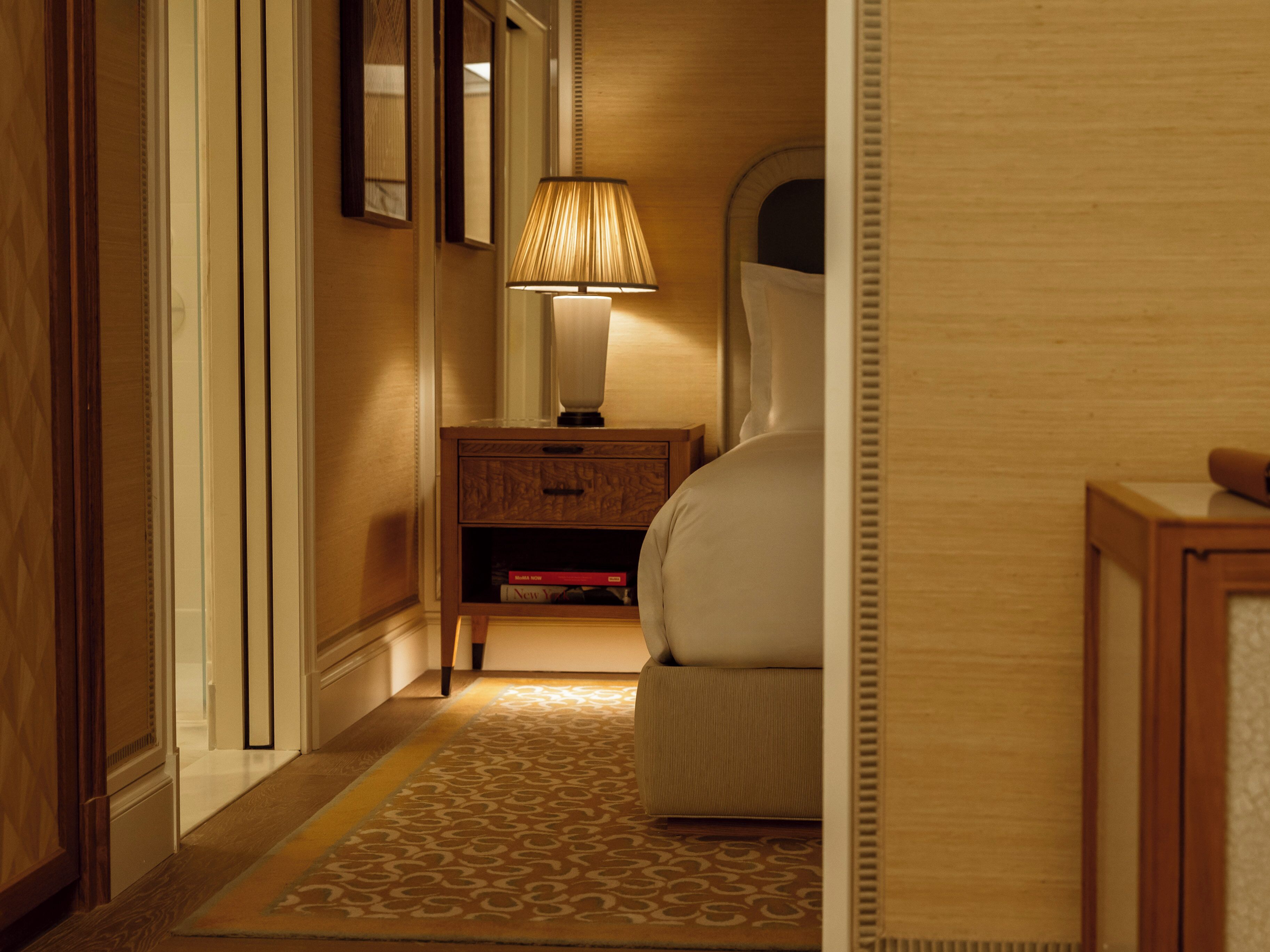 Una habitación de hotel con cama, mesita de noche, lámpara y un tapete estampado.
