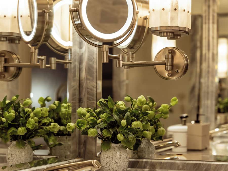 A bathroom with a large mirror, multiple lights, and a marble countertop.