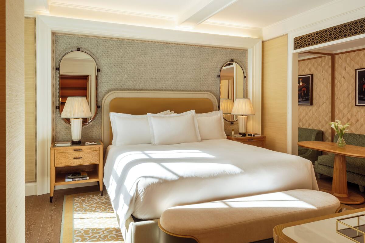 A hotel room with a large bed, two bedside tables with lamps, a small round table with a vase, and a green sofa.