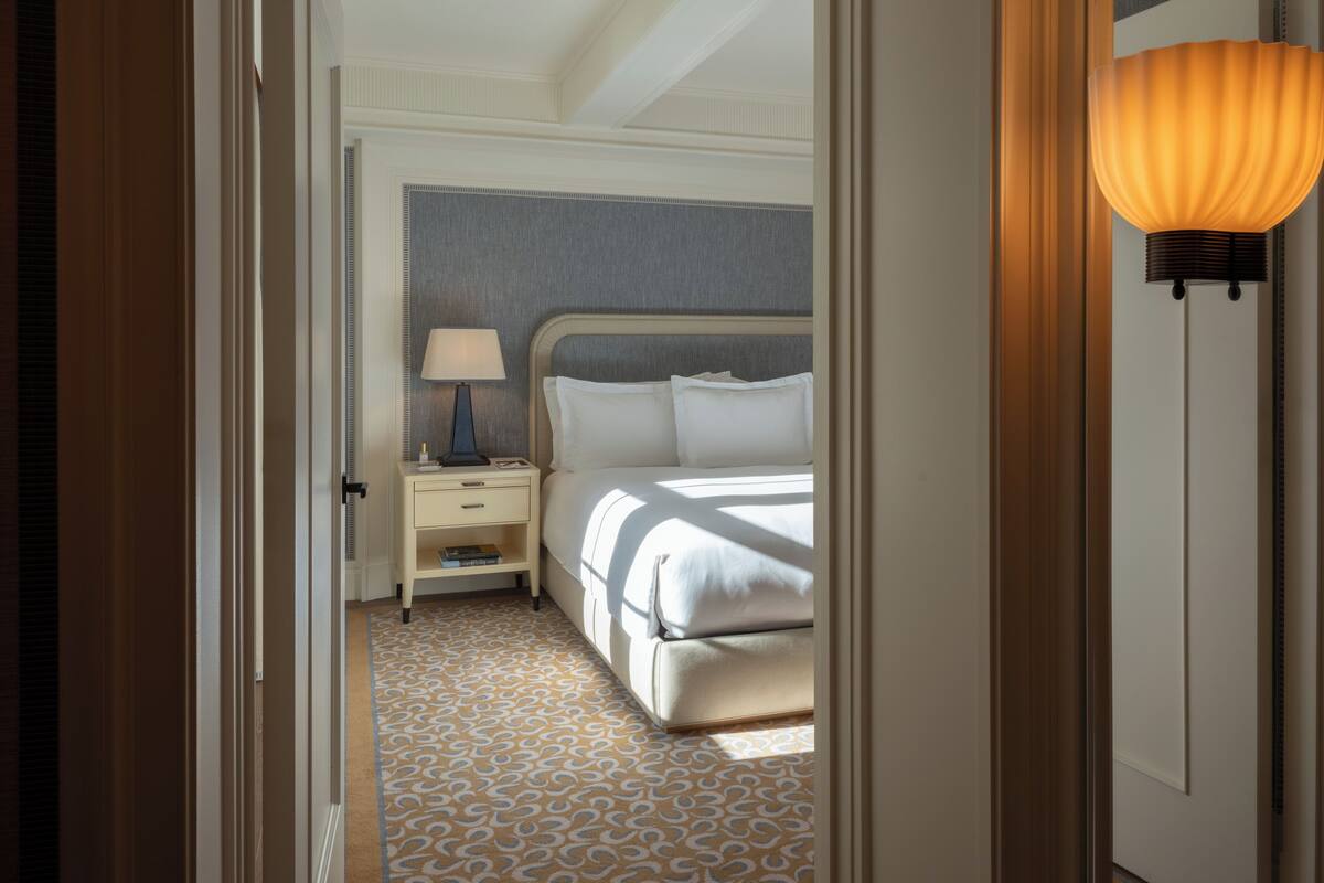 A hotel room with a bed, bedside table, lamp, and patterned carpet.