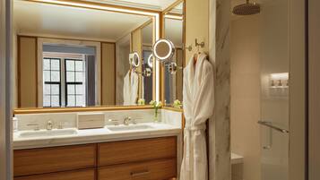 A modern bathroom with a large mirror, dual sinks, a robe hanging, and a shower area.