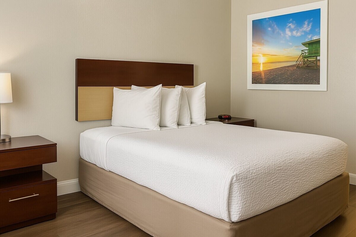 A neatly made bed with white bedding, a wooden headboard, and a nightstand with a lamp.