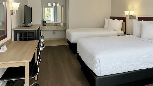 A hotel room with two beds, a desk, a TV, and a bathroom visible through an open door. - Days Inn by Wyndham Bradenton I-75 (Bradenton)