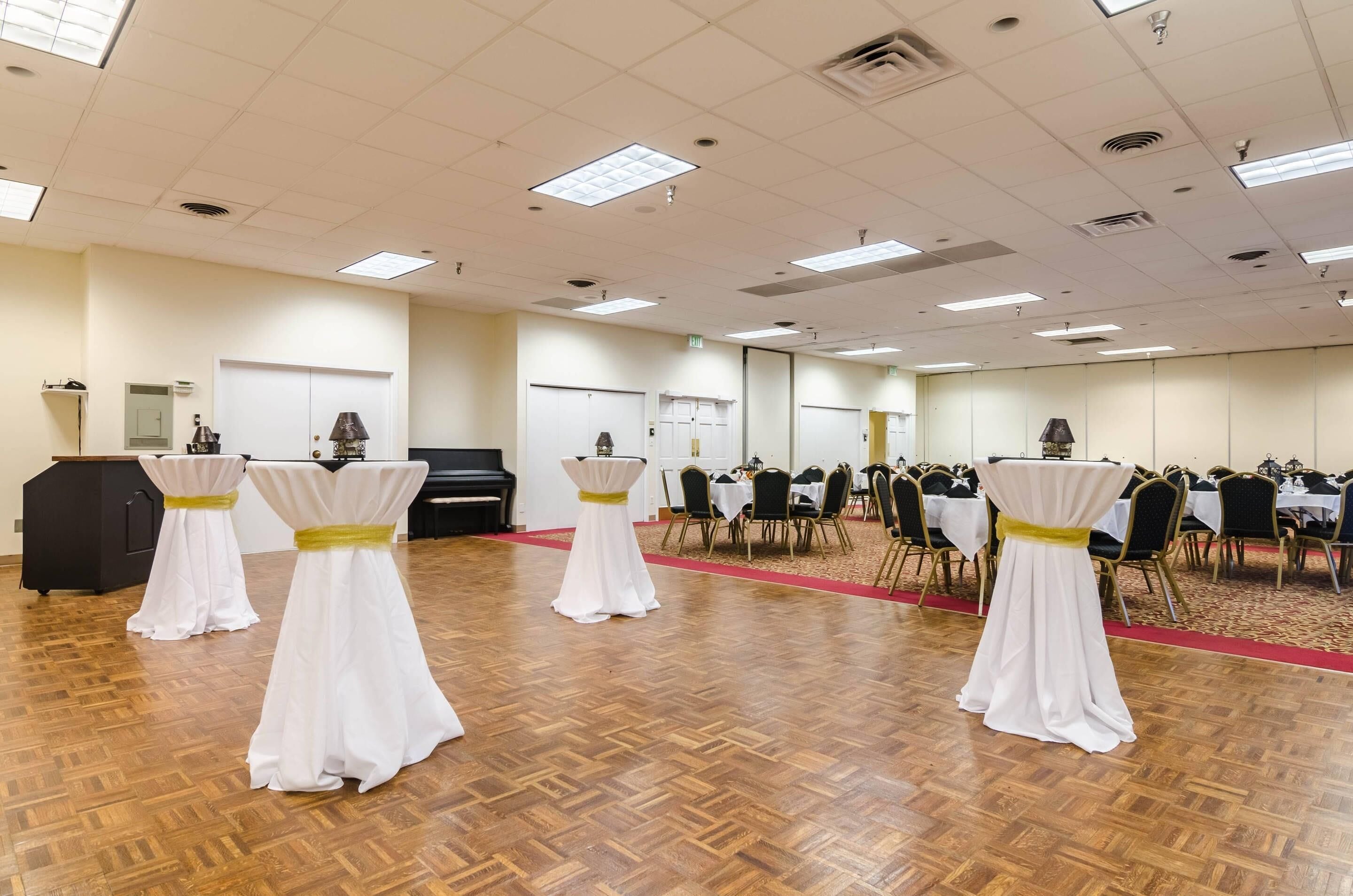 A conference room with white tables and chairs, a piano, and a carpeted floor.