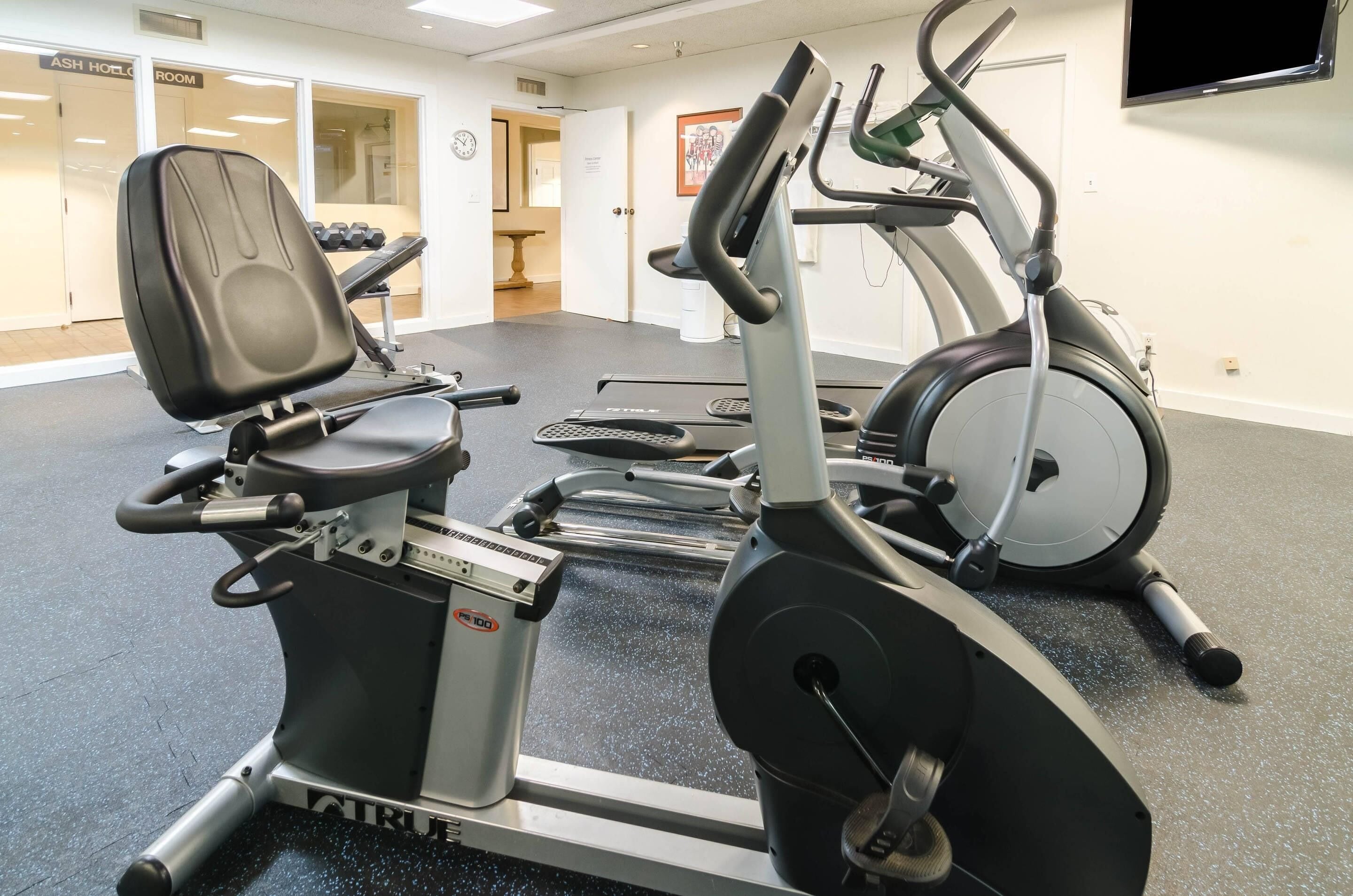 Un gimnasio con máquinas de cardio, una banca para pesas y mancuernas.
