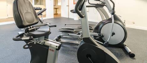 Un gimnasio con máquinas de cardio, una banca para pesas y mancuernas.