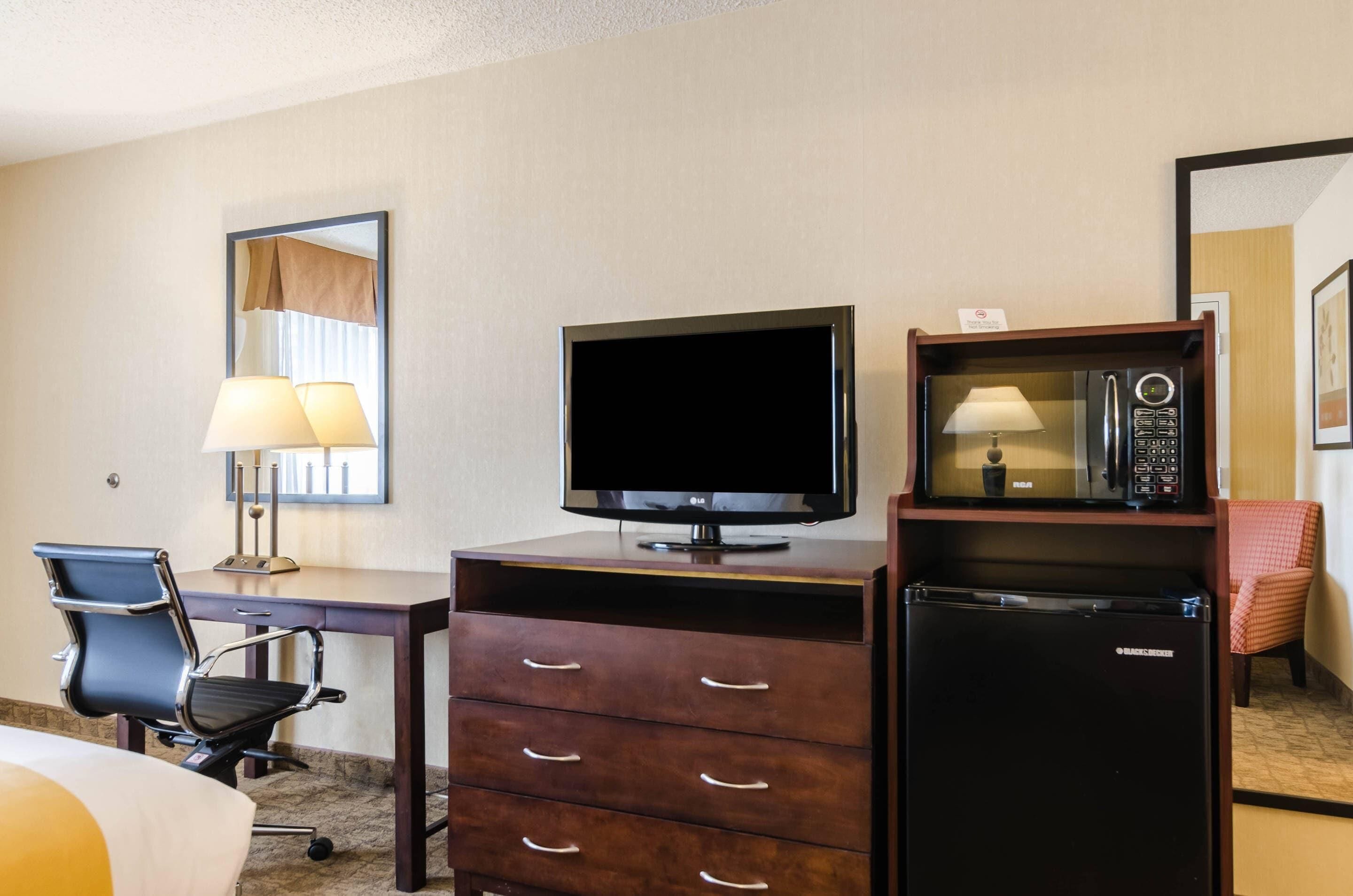 Ein Hotelzimmer mit Flachbildfernseher, Mikrowelle, Kühlschrank, Schreibtisch mit Stuhl und Bett.