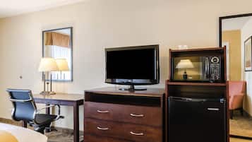 Habitación de hotel con televisión de pantalla plana, microondas, refrigerador, escritorio con silla y cama.
