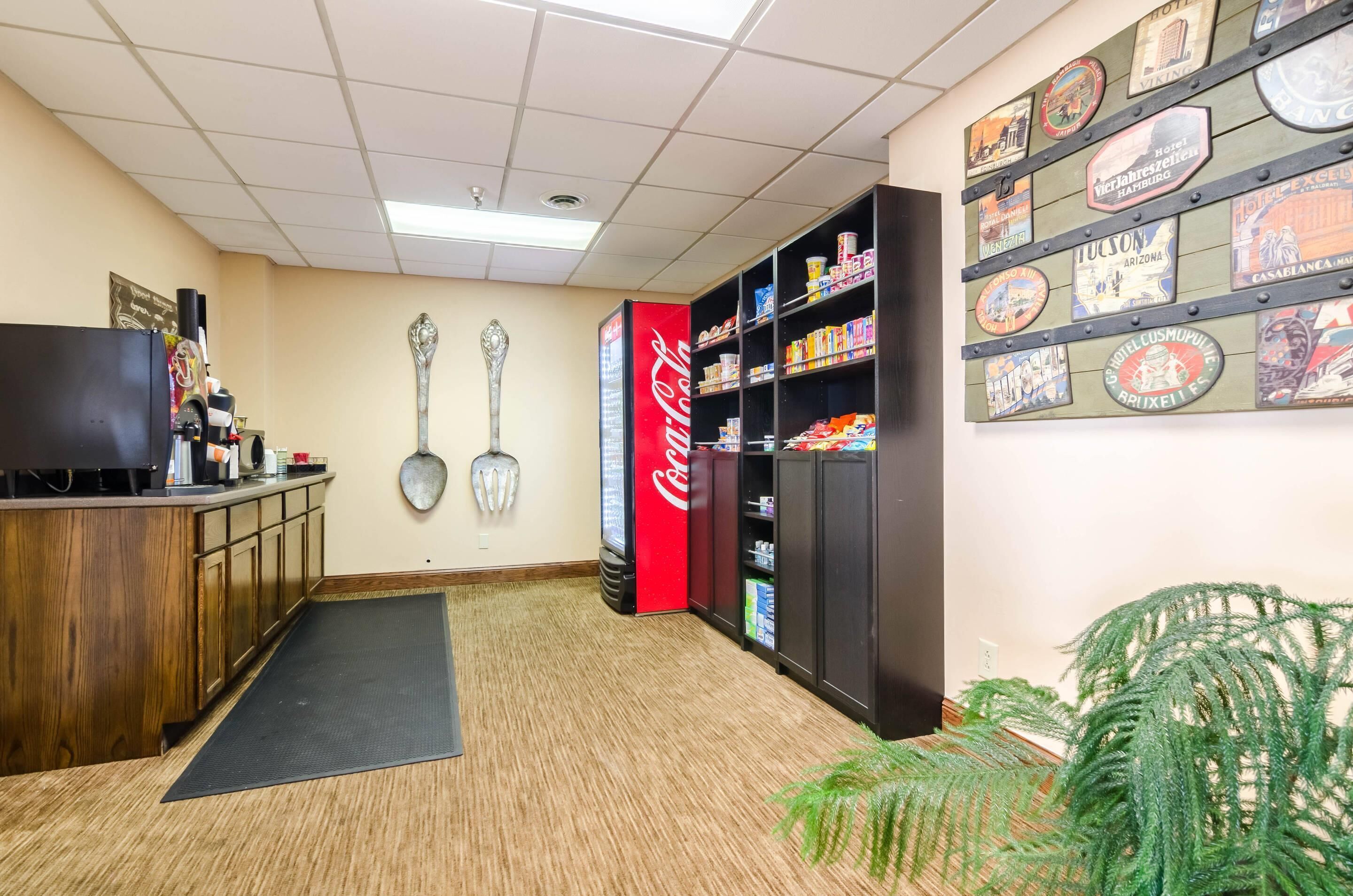 Zona de recepció d'hotel amb un taulell de fusta, una televisió, un refrigerador de Coca-Cola i una paret amb diferents plaques amb temàtica hotelera i urbana.