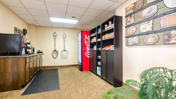 A hotel reception area with a wooden desk, a television, a Coca-Cola refrigerator, and a wall with various hotel and city-themed plaques.