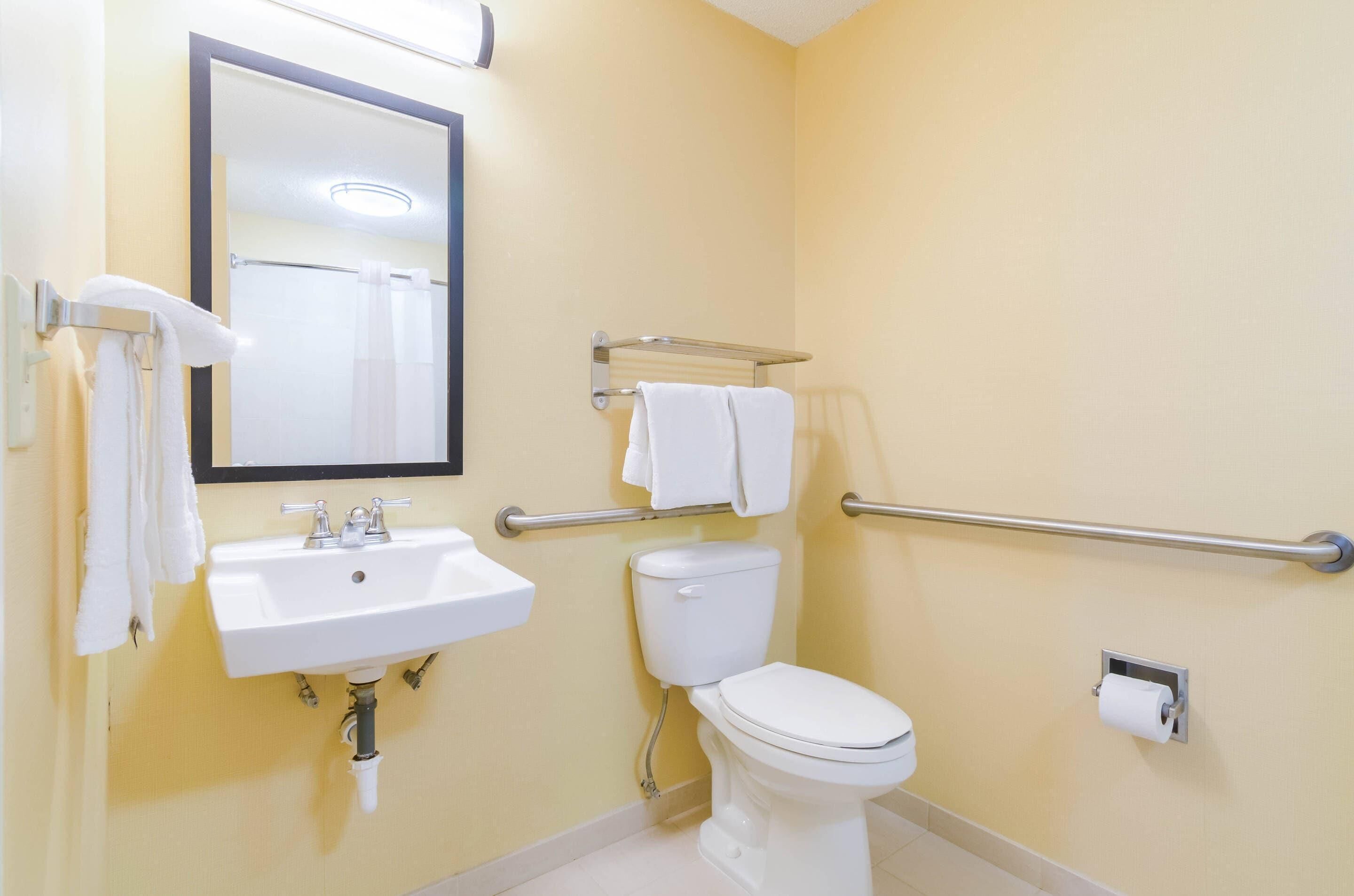 A bathroom with a white sink, a toilet, a mirror, and a towel rack.