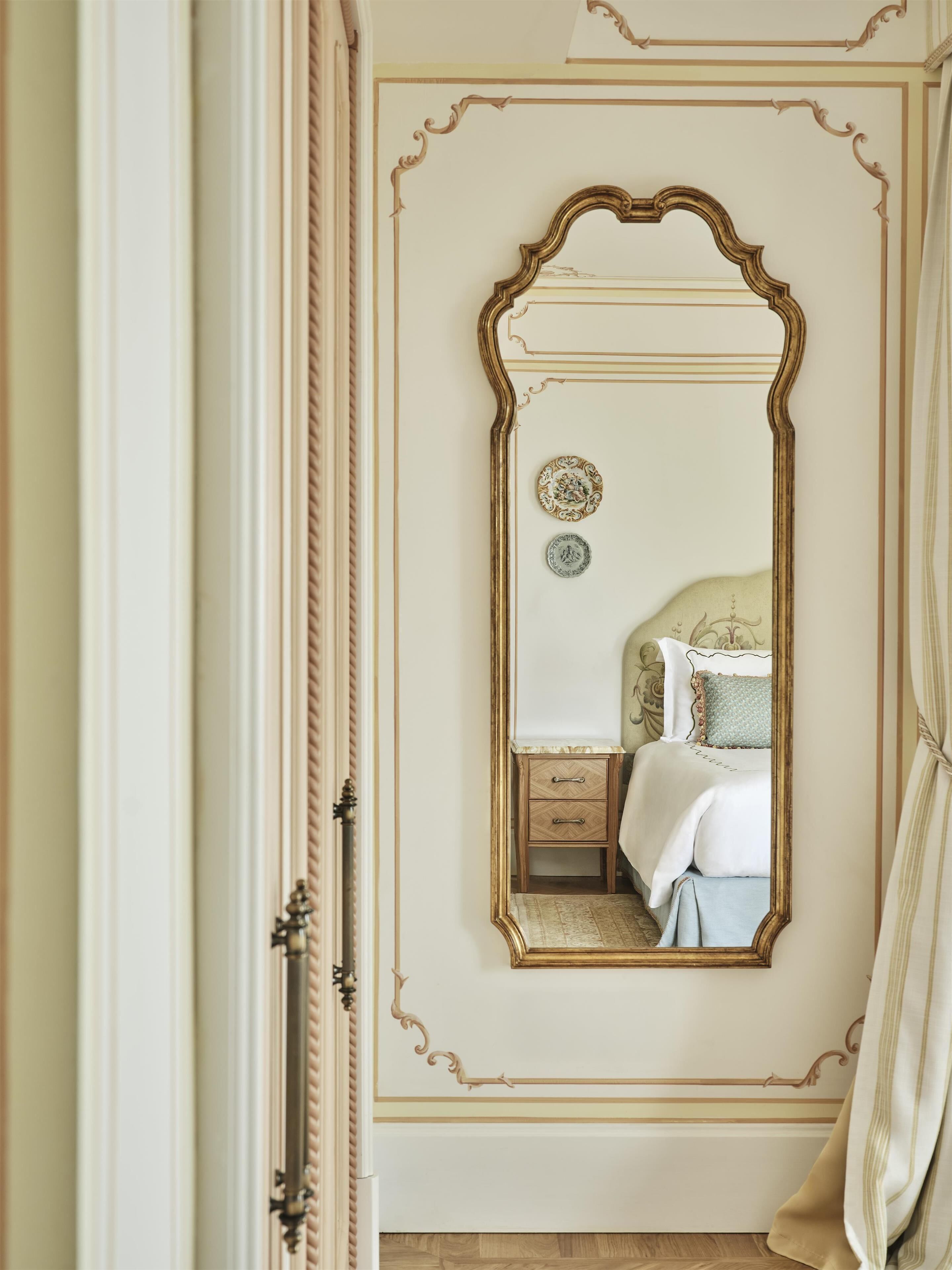 Una camera da letto con un grande specchio decorato, un letto con testiera bianca e un comodino con cassetti.