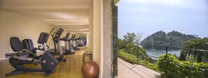 A gym with cardio machines and a large exercise ball, overlooking a scenic coastal view with boats and greenery.