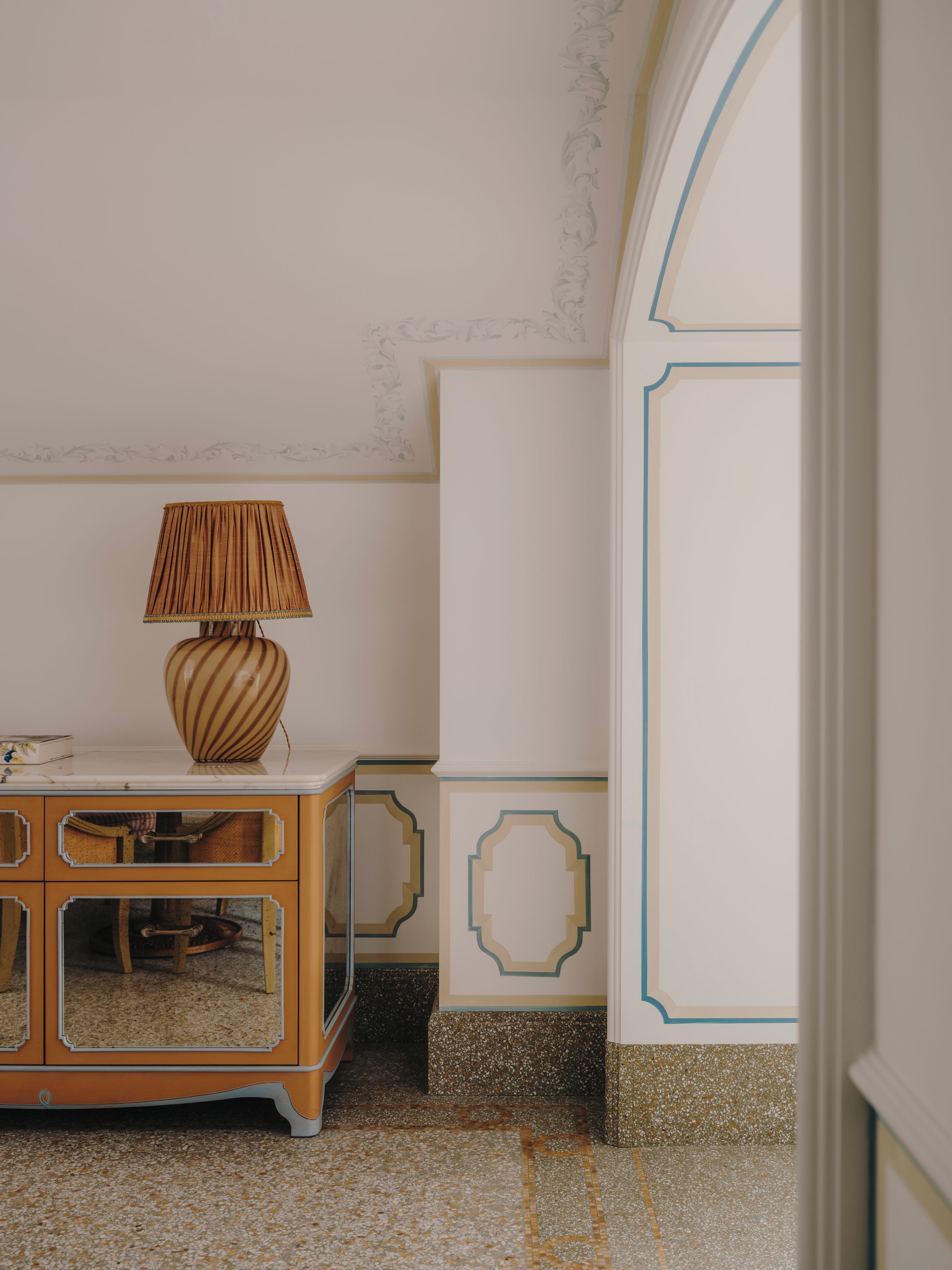 Une pièce avec un meuble en bois, une lampe et un mur décoratif orné de motifs géométriques.