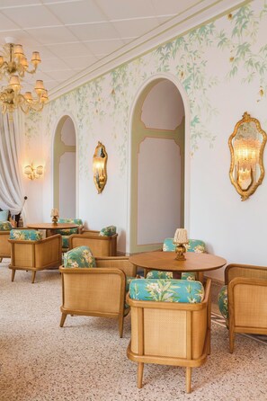 A room with a classic design, featuring a chandelier, floral wallpaper, and traditional furniture.