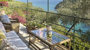 A covered outdoor seating area with wicker furniture, a glass table, and a view of the sea and hills. - Splendido, A Belmond Hotel, Portofino (Portofino)