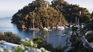 A coastal town with boats docked along the shore, a prominent hill with a building on top, and a road leading up to the hill. - Splendido, A Belmond Hotel, Portofino (Portofino)