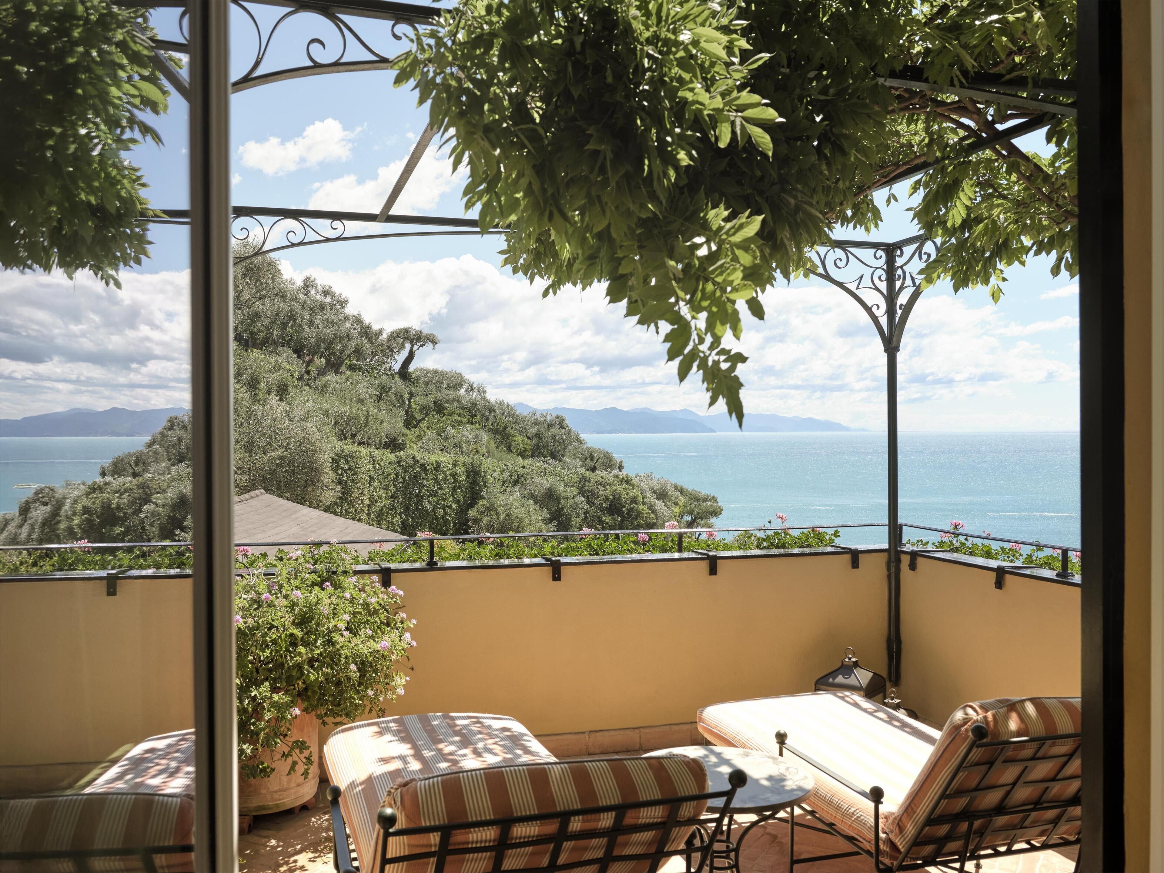 Un balcone con vista sul mare, una pianta in vaso e una zona relax con tavolo e sedie.