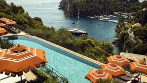 A swimming pool with lounge chairs and umbrellas, overlooking a marina with boats and a forested island. - Splendido, A Belmond Hotel, Portofino (Portofino)