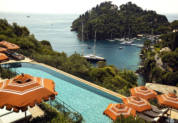 A swimming pool with lounge chairs and umbrellas, overlooking a marina with boats and a forested island. - Splendido, A Belmond Hotel, Portofino (Portofino)