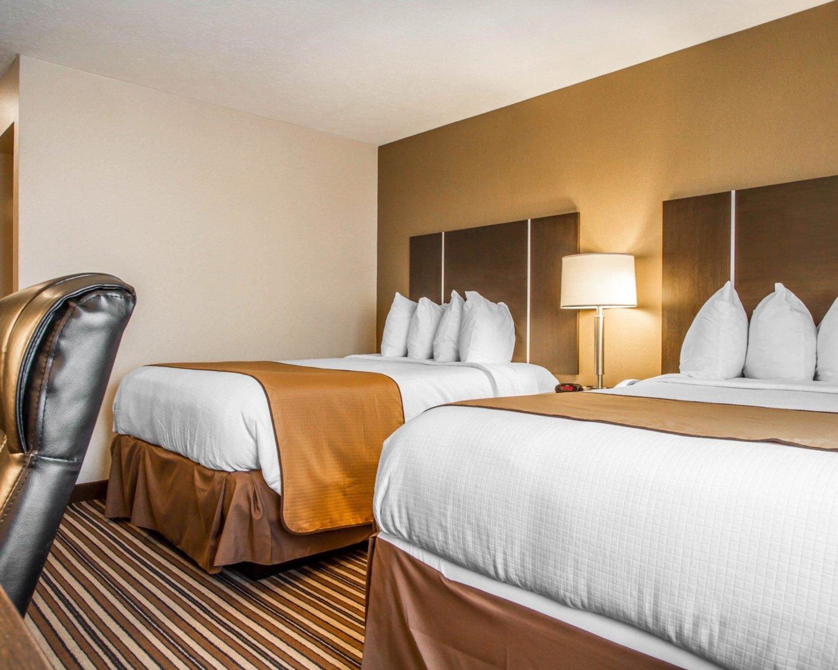 A hotel room with two beds, a leather chair, a lamp, and a striped carpet.