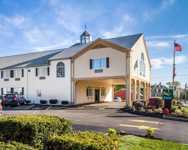 Classic motel with a covered porch and a charming entrance, set amidst beautifully maintained gardens.