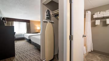 Habitación de hotel con cama, tabla de planchar, zona de ducha y perchero.
