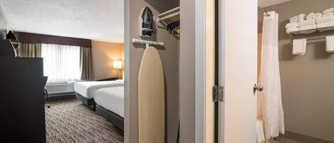 A hotel room with a bed, an ironing board, a shower area, and a towel rack.