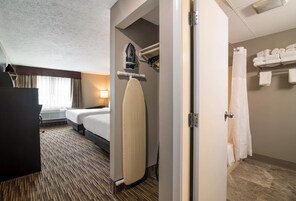 Habitación de hotel con cama, tabla de planchar, zona de ducha y perchero.