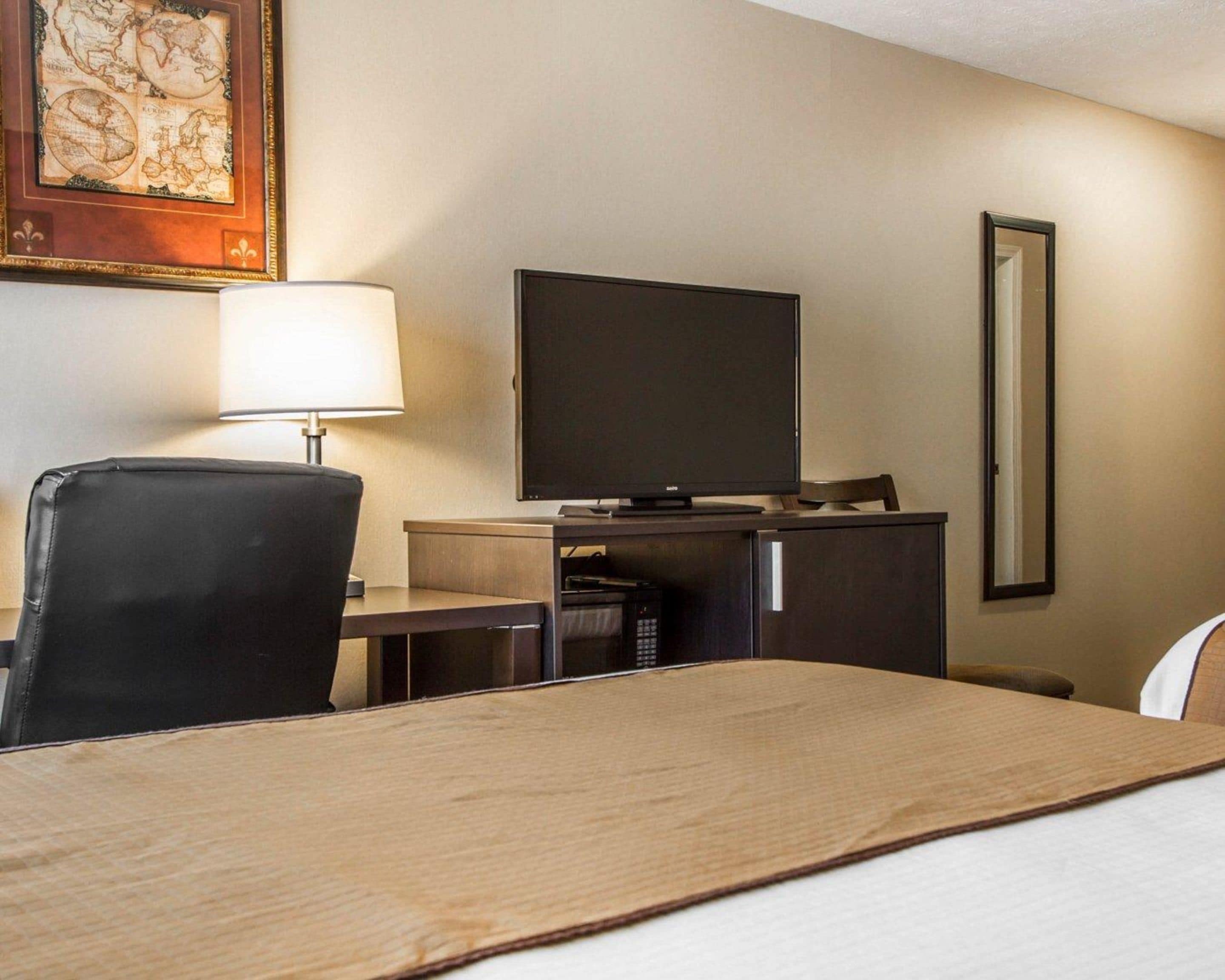 A hotel room with a bed, a desk with a television, a chair, and a lamp.