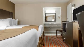 Een hotelkamer met twee bedden, een bureau, een televisie, een spiegel en een badkamer met een wastafel en spiegel.