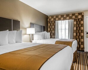 A hotel room with two beds, a nightstand, a lamp, and a window with curtains.