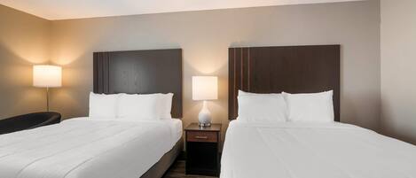 Habitación de hotel con dos camas, cada una con ropa blanca, cabeceros oscuros y una lámpara de noche.