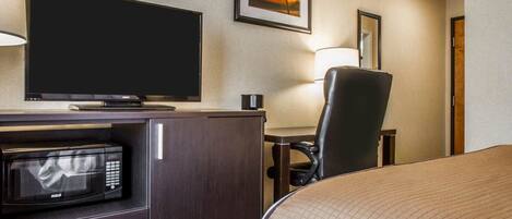 Ein Hotelzimmer mit Bett, Fernseher, Mikrowelle, Schreibtisch mit Stuhl und einem gerahmten Bild an der Wand.