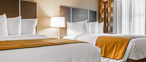 A hotel room with two beds, a nightstand, a lamp, and a window with curtains.