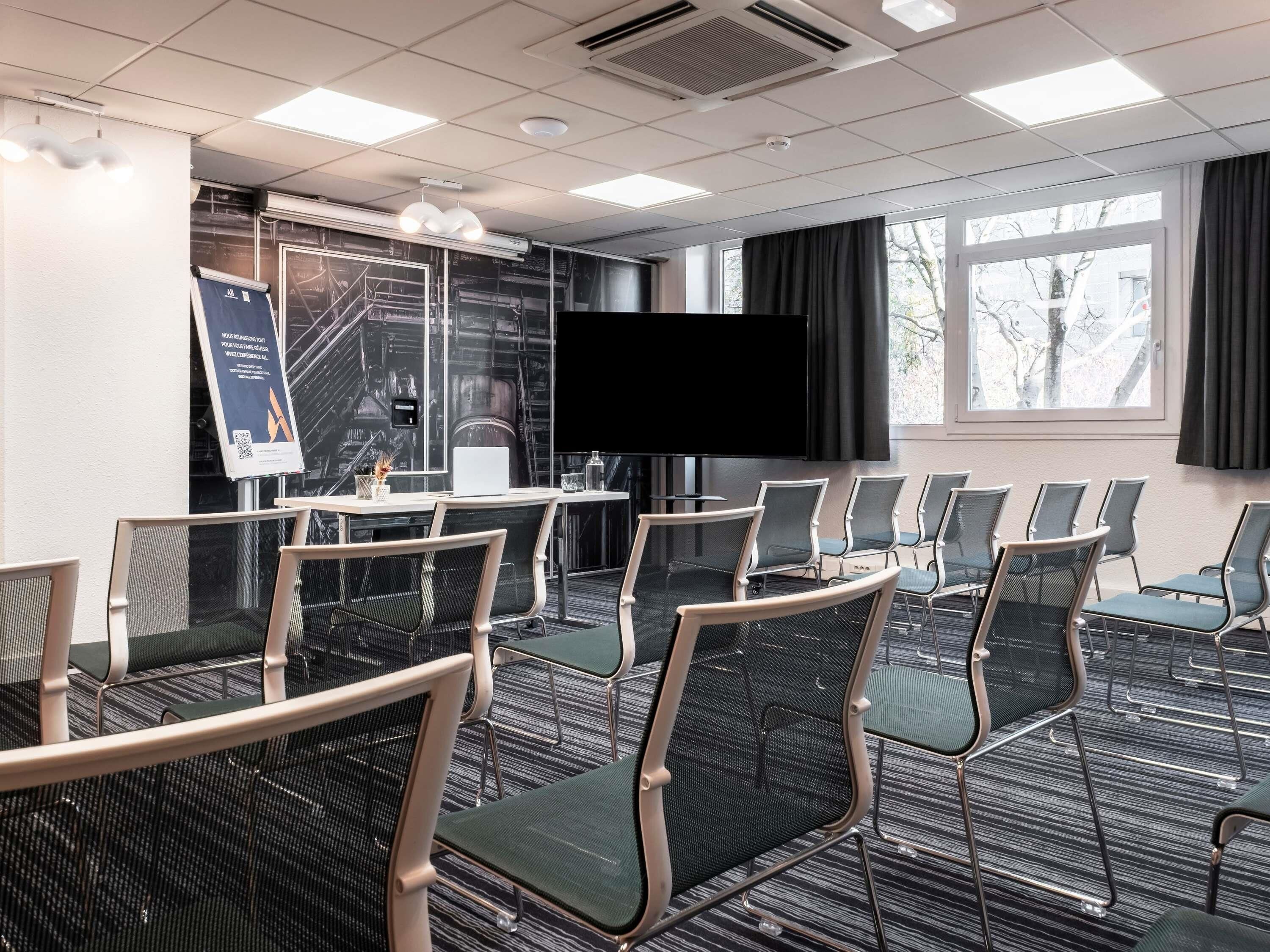 A conference room with a large flat-screen TV, rows of chairs, a table with a laptop, and a poster on the wall.