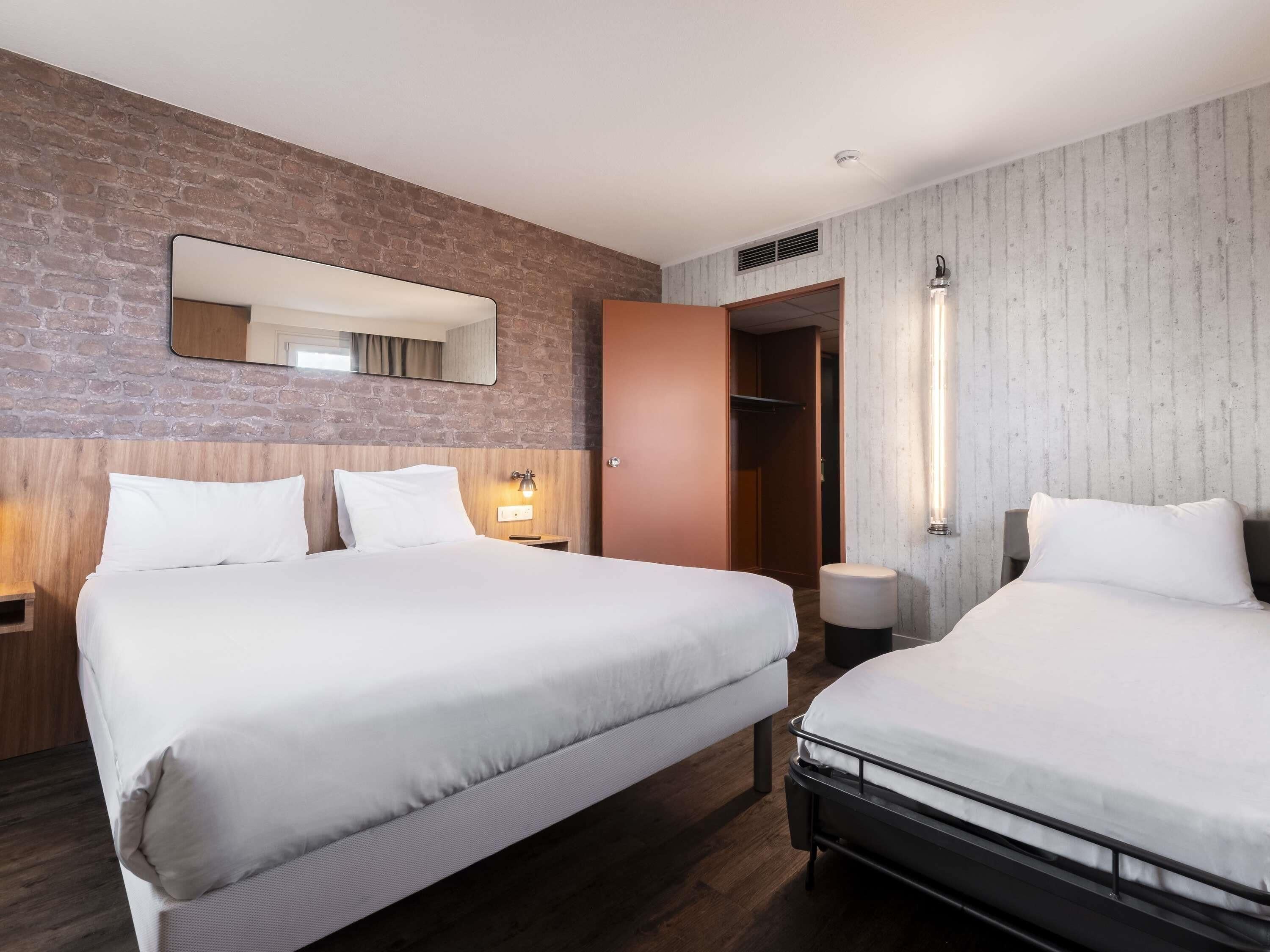 Une chambre d’hôtel avec un grand lit, une table de chevet, une commode, un miroir, une armoire et un luminaire fixé au mur.