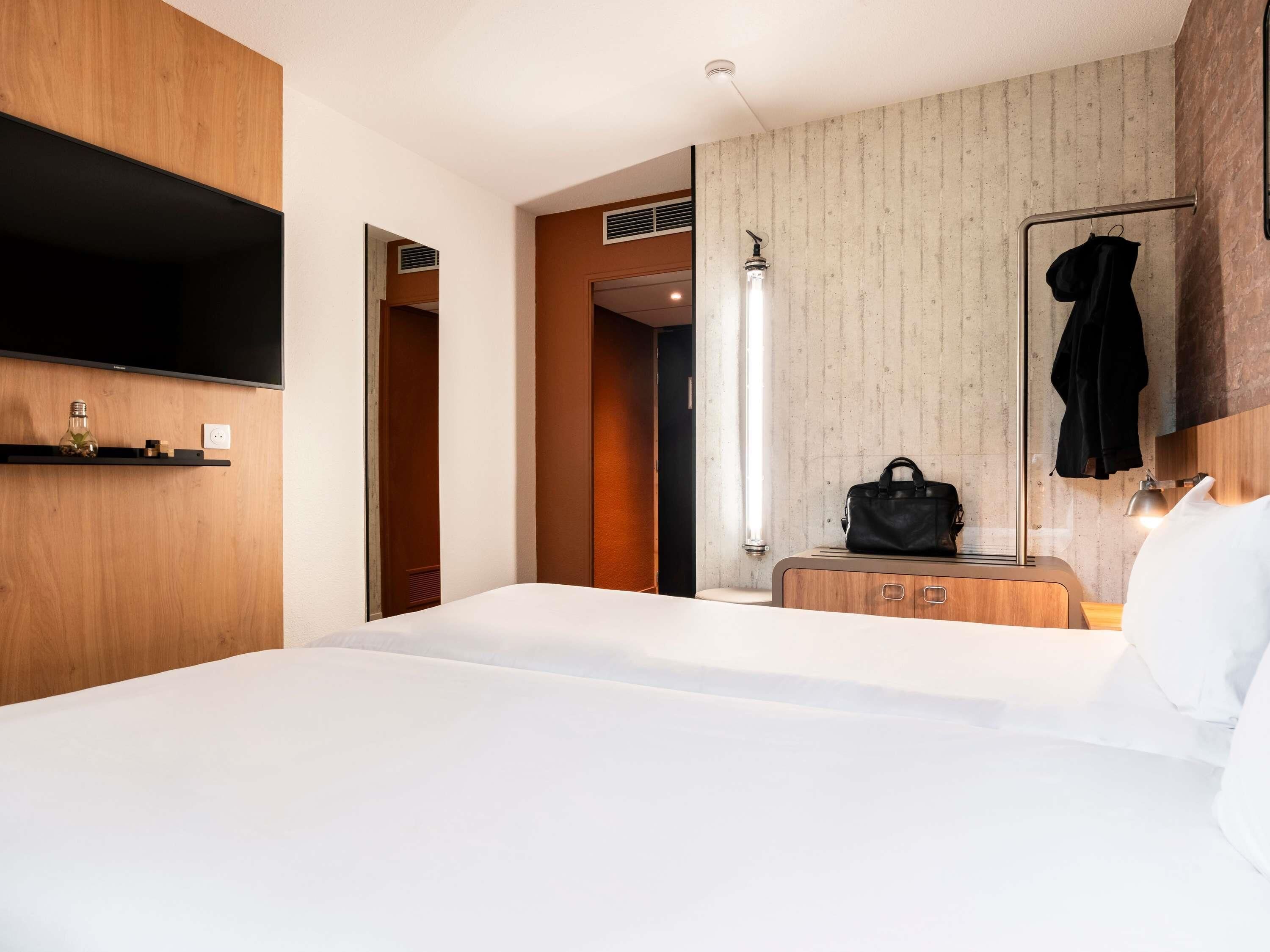 Camera d'albergo con un letto grande, una TV fissata al muro, un comò in legno e uno specchio con un accappatoio appeso.